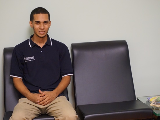 Adolescent male with short hair sits on a chair. 